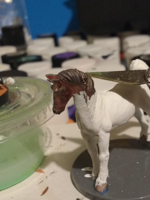 An inexpensive toy horse with an exacto knife poised to cut off it's head.